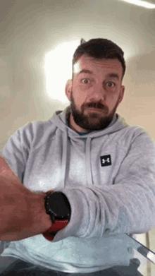 a man with a beard wearing a grey under armour hoodie and a smart watch .