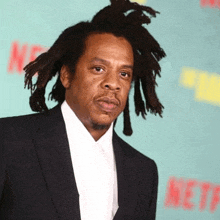 a man in a suit and tie with dreadlocks is standing on a green carpet .