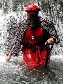 a woman in a red dress and leopard print jacket is standing in a waterfall