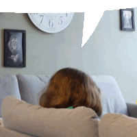 a woman sits on a couch in front of a wall clock that shows the time as 6:55