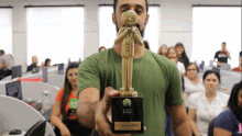 a man in a green shirt is holding a trophy in front of a group of people in an office