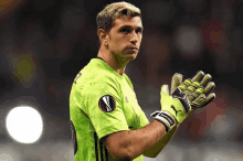 a soccer player wearing a green jersey and yellow gloves stands on the field .