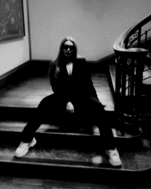 a woman in a black suit sits on a set of stairs with her legs crossed