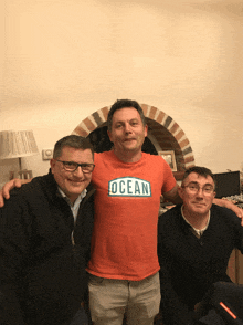 three men are posing for a picture with one wearing an orange shirt that says ocean