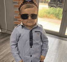 a little boy wearing sunglasses and a striped shirt with the letter a on the collar