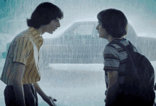 two young men are standing next to each other in the rain looking at each other .