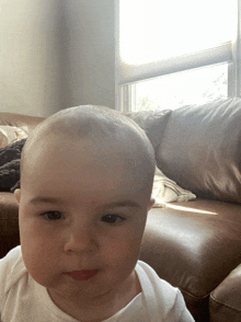 a baby with a shaved head is sitting on a couch