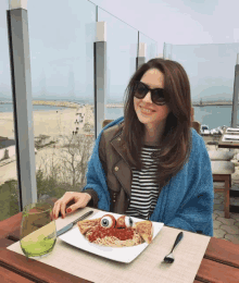 a woman wearing sunglasses sits at a table with a plate of food that looks like a monster with an eye on it