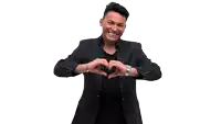 a man in a black jacket and black shirt making a heart shape with his hands