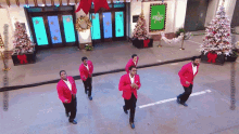 a group of men in red jackets are dancing on a street in front of a building that says abc