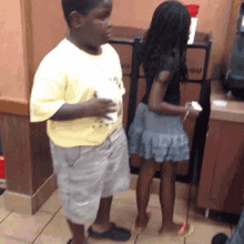 a boy and a girl are standing next to each other in a restaurant . the girl is wearing a skirt .