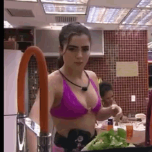 a woman in a purple bikini is standing next to a sink in a kitchen .