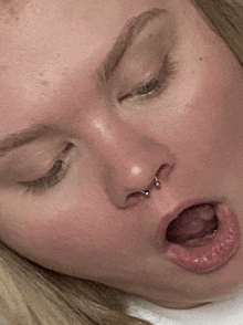 a close up of a woman 's face with a nose ring and her mouth open