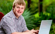 a young man with down syndrome is typing on a laptop computer .