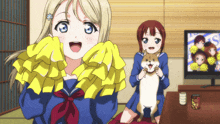 a cheerleader holds a dog while another cheerleader looks on in front of a tv