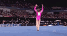 a female gymnast in a pink leotard is doing a trick on the floor in front of a crowd .