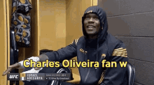 a man in a hooded jacket is sitting in a locker room with the words charles oliveira fan w written on the screen