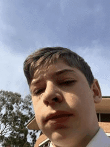 a young boy in a white shirt is taking a selfie with a blue sky in the background .