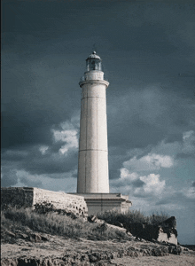 a lighthouse on a rocky hillside with a cloudy sky in the background