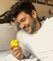 a man in a white shirt is holding a yellow ball with a smiley face on it .