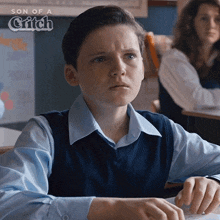 a young boy is sitting at a desk in a classroom with the words son of a gritch behind him