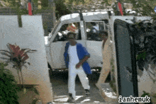 a man in a blue jacket and white pants is walking in front of a white van and a sign that says iamhamuk