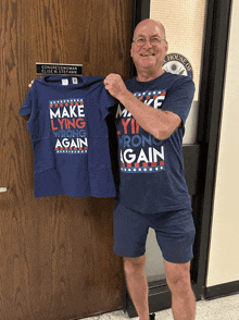 a man holding up a blue shirt that says make lying wrong again