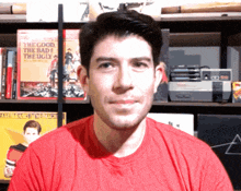 a man wearing a red shirt is standing in front of a bookshelf with a book titled the good the bad and the ugly