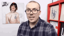 a man wearing glasses stands in front of a picture of a shirtless man with the words total anarchy on it