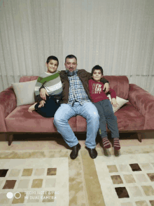 a man sits on a couch with two boys one of whom is wearing a red shirt that says new york