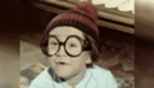 a young boy wearing glasses and a beanie is making a funny face .