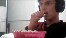 a young man wearing headphones eating popcorn from a pink bowl