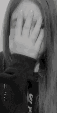 a black and white photo of a girl covering her face with her hand .