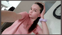 a girl in a pink shirt taking a selfie with a clock in the background