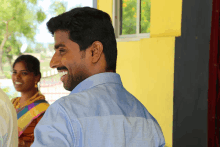 a man in a blue shirt smiles with a woman behind him