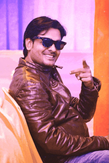 a man wearing sunglasses and a brown leather jacket smiles