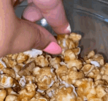 a close up of a person 's hand dipping a piece of popcorn into a bowl of caramel popcorn .