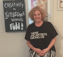 a woman is standing in front of a sign that says creativity is intelligence having fun