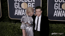 a man and a woman pose on a red carpet in front of a sign that says golden globe award