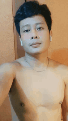 a shirtless man wearing ear buds and a necklace takes a selfie