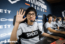 a man wearing headphones and a shock shirt waves his hand