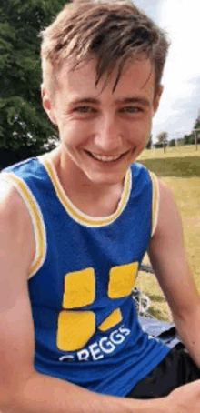 a young man wearing a blue and yellow peggs tank top is smiling