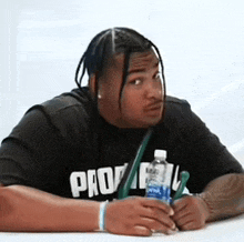 a man wearing a black shirt with the word pro on it is sitting at a table holding a bottle of water