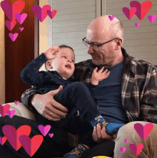 a man is holding a small child in his arms while sitting on a couch surrounded by hearts .