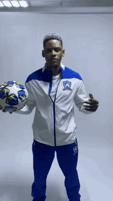 a man holding a soccer ball wearing a blue and white jacket