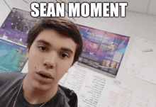 a young man is standing in front of a wall with a poster that says sean moment