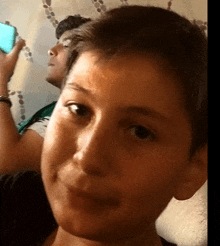 a close up of a young boy 's face with a man behind him holding a blue cell phone