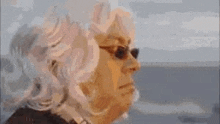 a close up of a woman wearing sunglasses and a wig looking out a window .