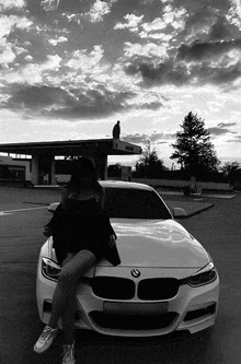 a black and white photo of a woman sitting on the front of a white bmw .