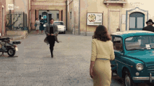 a woman in a yellow dress stands in front of a blue car in front of a sign that says barbieri